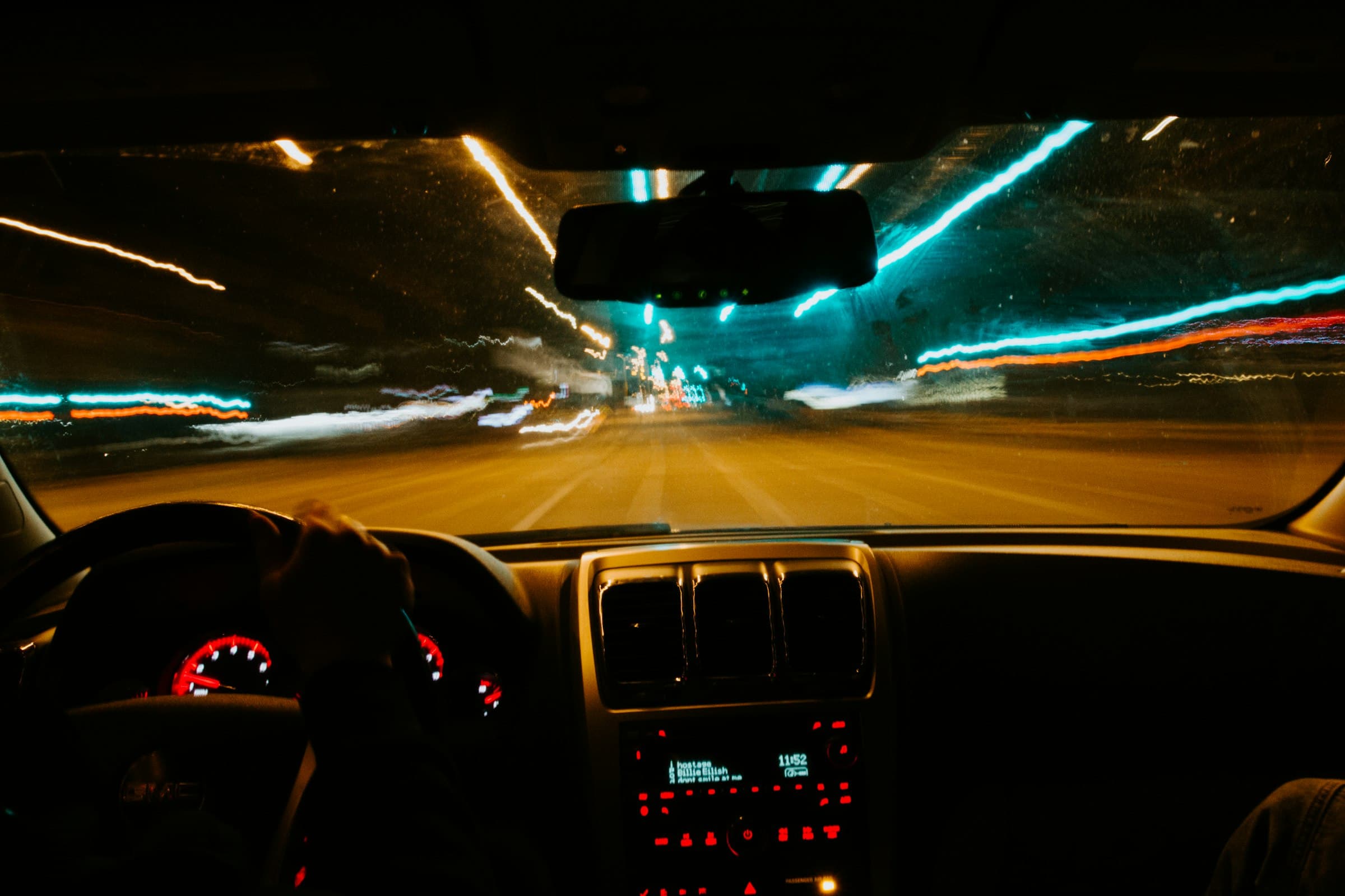 Driver's view from inside a car at night, city lights streaking past
