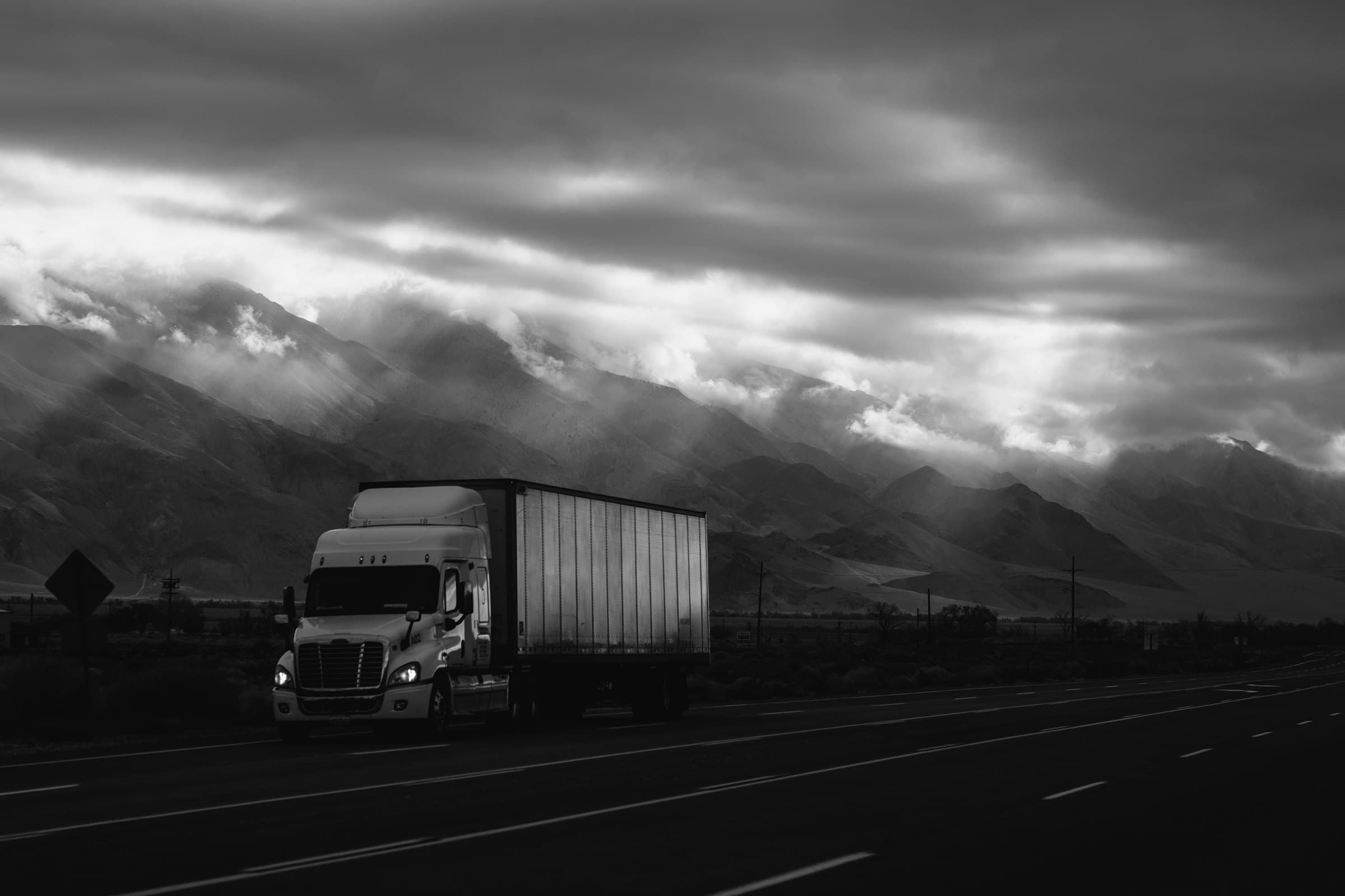 Semi truck on a highway beneath storm clouds and rays of light